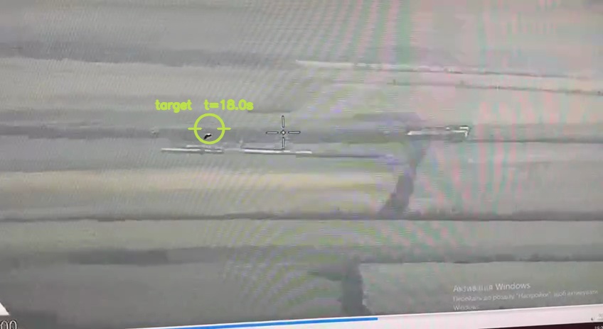 A rural aerial view with a small airborne target circled left of the reticle.
